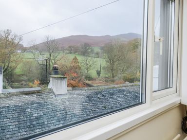 A window view showing rooftops trees and hills in the background at Holme Rigg in Braithwaite