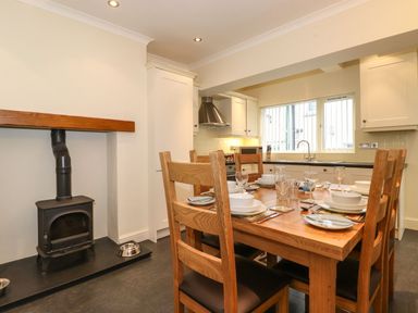 A kitchen dining area with wooden table and chairs next to a black wood burning stove at Holme Rigg in Braithwaite