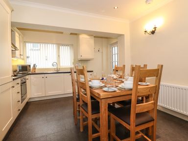 A kitchen and dining area with wooden dining table and chairs set with plates and glasses at Holme Rigg in Braithwaite