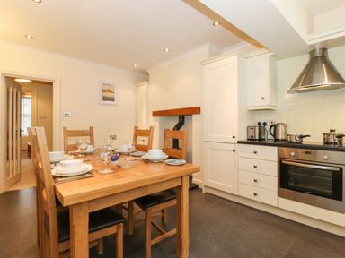 A kitchen with a wooden dining table and six chairs and white cabinetry with an oven and cooker hood at Holme Rigg in Braithwaite