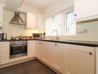 A kitchen with white cabinets a stainless steel oven a microwave and a window with vertical blinds at Holme Rigg in Braithwaite