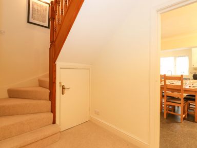 Stairs with carpet and a small door underneath next to a dining area with wooden chairs at Holme Rigg in Braithwaite