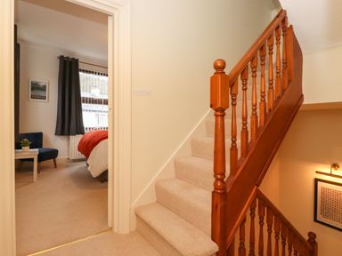 A carpeted staircase with wooden banisters next to a bedroom with a bed red blanket and dark curtains at Holme Rigg in Braithwaite