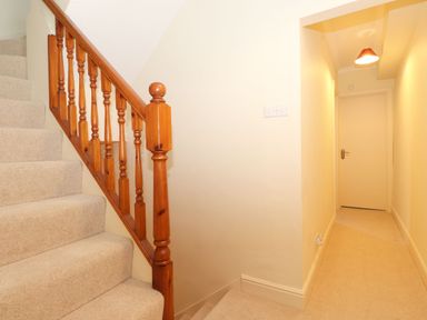 A carpeted staircase with wooden railing next to a narrow hallway with a closed door at Holme Rigg in Braithwaite