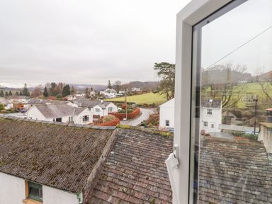 A village view with white houses roofs and green fields seen through an open window at Holme Rigg in Braithwaite