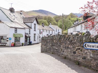 Village street with white houses a stone wall and a shop with a green awning at Holme Rigg in Braithwaite