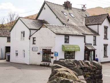 White stone buildings with slate roofs and signs for The Village Shop on a street corner with a dry stone wall in foreground at Holme Rigg in Braithwaite