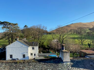 A white house with a slate roof near grassy hills and trees at Holme Rigg in Braithwaite