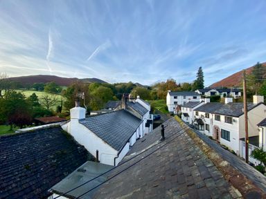 A view of rooftops of white houses with chimneys and green hills in the background at Holme Rigg in Braithwaite