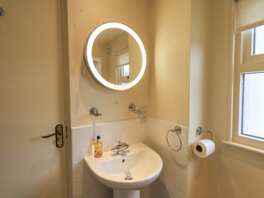 A bathroom sink with a round illuminated mirror a soap dispenser a towel ring and a toilet paper holder near a frosted window at Holme Rigg in Braithwaite