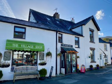 An exterior view of a village shop with a green awning and a wooden bench outside at The Village Shop in Braithwaite
