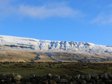 A landscape with a stone wall in the foreground grassy fields and snow-covered hills under a blue sky at Fig Cottage in Kirkby Stephen