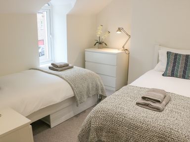 A bedroom with two single beds with blankets and towels a dresser with a lamp and flower at Fig Cottage in Kirkby Stephen