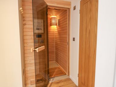 An open wooden sauna room with a glass door and a light fixture inside at Fig Cottage in Kirkby Stephen