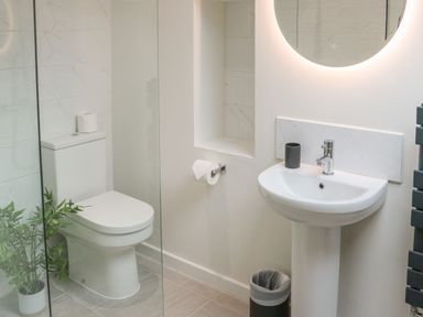 A bathroom with a toilet a sink a circular mirror and a small plant at Fig Cottage in Kirkby Stephen