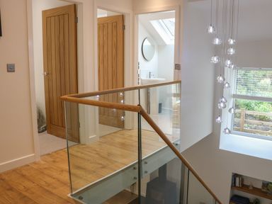 A hallway with wooden doors glass railing and a bathroom with a round mirror at Fig Cottage in Kirkby Stephen
