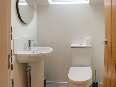 A bathroom with a white sink and round mirror next to a white toilet with a roll of toilet paper on top at Fig Cottage in Kirkby Stephen