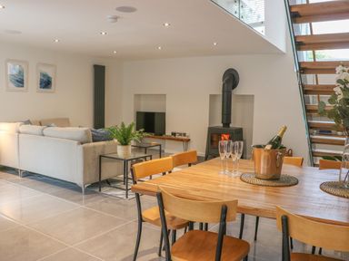 A dining area with wooden table and chairs adjacent to a living room with a sofa a wood stove and stairs at Fig Cottage in Kirkby Stephen