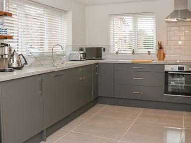 A modern kitchen with grey cabinets a stainless steel oven microwave toaster coffee maker and dish rack at Fig Cottage in Kirkby Stephen