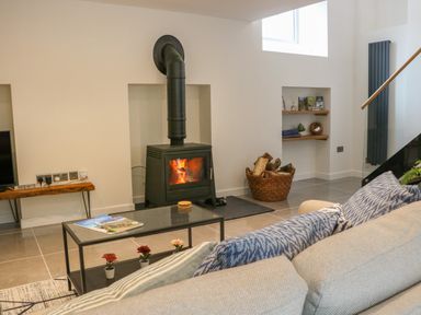 A living room with a wood burning stove a glass coffee table a light sofa and a basket of firewood at Fig Cottage in Kirkby Stephen