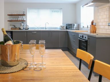 A kitchen with a wooden table set with glasses and a champagne bottle in a bucket at Fig Cottage in Kirkby Stephen