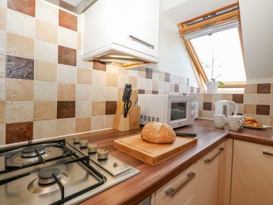 A kitchen counter with a loaf of bread on a wooden cutting board a white microwave a kettle two mugs and a knife block under a window at Harbour Reach 6 in Weymouth