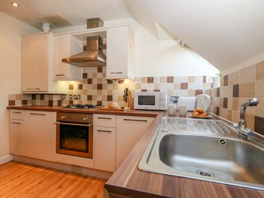 A kitchen with white cabinets a stove a microwave a toaster a kettle and a sink at Harbour Reach 6 in Weymouth