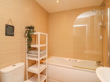 A bathroom with a bathtub and shower curtain a white shelf unit with towels and a plant and a toilet at Harbour Reach 6 in Weymouth