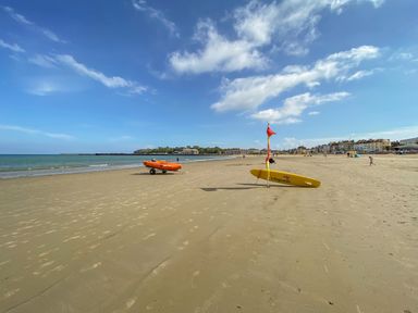 A sandy beach with a lifeguard board and an inflatable boat near the shoreline at Harbour Reach 6 Weymouth