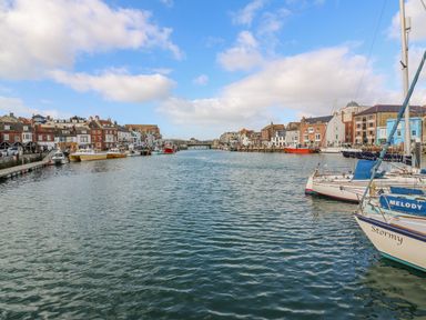 A harbor with boats docked along the sides and buildings lining the waterfront at Harbour Reach 6 in Weymouth