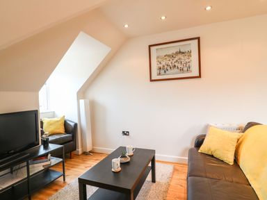 A living room with a television on a stand a black coffee table with cups and a plant and sofas with yellow cushions at Harbour Reach 6 in Weymouth