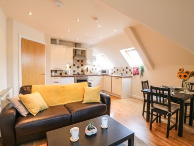 A kitchen and dining area with a brown sofa and yellow cushions at Harbour Reach 6 in Weymouth
