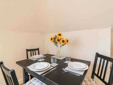 A dining table set for four with plates glasses silverware and a vase of sunflowers at Harbour Reach 6 Weymouth