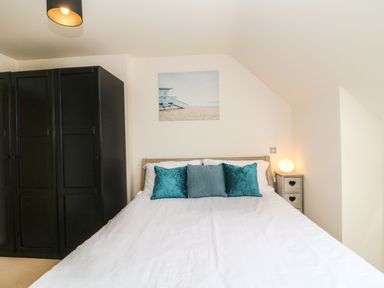 A bedroom with a bed with white bedding and three blue pillows a black wardrobe and a nightstand with a lamp at Harbour Reach 6 Weymouth