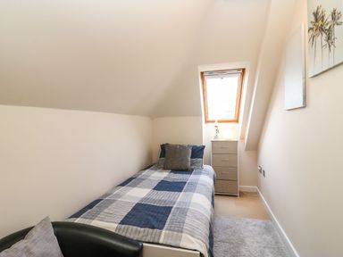 A small bedroom with a single bed a window a chest of drawers a chair and wall art at Harbour Reach 6 in Weymouth