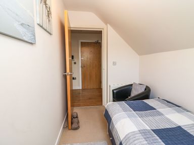 A bedroom with a bed covered in a checkered blanket a black armchair a wooden door and paintings on the wall at Harbour Reach 6 in Weymouth