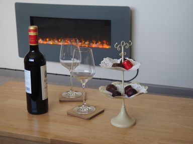 A bottle of wine two empty wine glasses chocolates on a stand and an electric fireplace in a living room at Berwyn View in Trelydan near Welshpool
