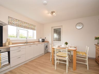 A kitchen with white cabinets a wooden dining table with chairs and a window with patterned blind at Berwyn View in Trelydan near Welshpool