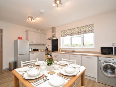 A kitchen with a dining table set with plates and cutlery next to appliances including a refrigerator and washing machine at Berwyn View in Trelydan near Welshpool