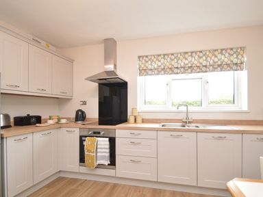 A kitchen with cupboards an oven a stove a kettle a sink and a window with a patterned blind at Berwyn View in Trelydan near Welshpool