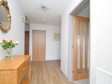 A hallway with wooden doors a wooden console table with a glass vase of flowers and a round mirror on the wall at Berwyn View in Trelydan near Welshpool