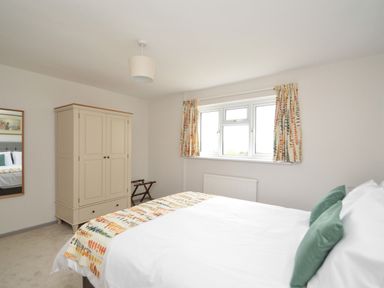 A bedroom with a double bed green pillows a wardrobe window with patterned curtains and a mirror on the wall at Berwyn View in Trelydan near Welshpool