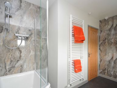 A bathroom with a shower area having marble-textured walls and two orange towels hanging on a white towel radiator at Berwyn View in Trelydan near Welshpool