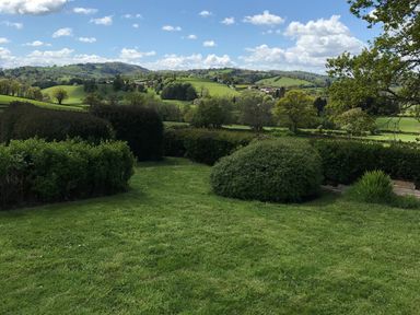 A grassy garden with bushes and trees overlooking green hills and scattered houses at Berwyn View in Trelydan near Welshpool