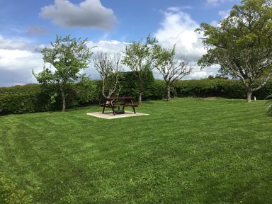 A picnic table on a concrete slab in a grassy garden with trees and hedges at Berwyn View in Trelydan near Welshpool