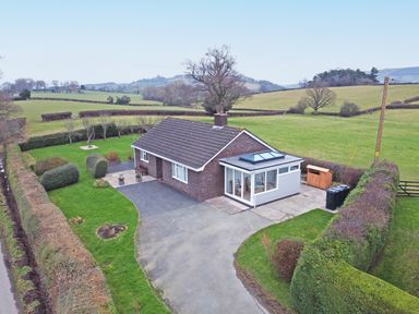 A single-story house with a driveway and surrounding hedges in a rural setting at Berwyn View in Trelydan near Welshpool