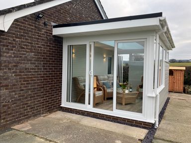 A glass sunroom with wicker chairs and a table with flowers and wine outside a brick house at Berwyn View in Trelydan near Welshpool