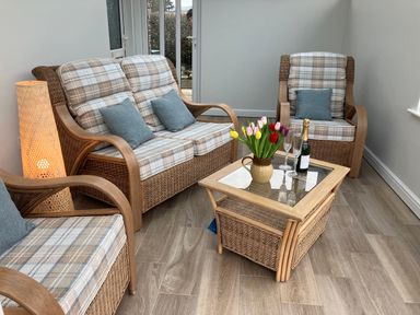 A sitting area with wicker armchairs and a loveseat with plaid cushions and a glass top wicker coffee table with flowers and wine at Berwyn View in Trelydan near Welshpool