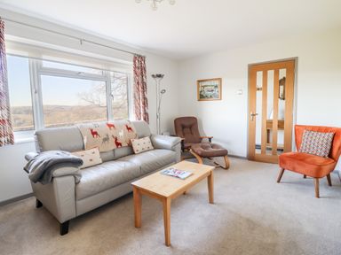 A living room with a grey sofa a brown reclining chair an orange armchair and a wooden coffee table at Berwyn View in Trelydan near Welshpool