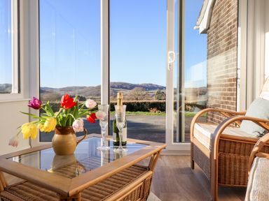 A sunroom with wicker furniture a glass table with flowers a bottle of champagne and two glasses at Berwyn View in Trelydan near Welshpool